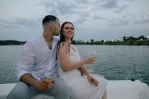 Joyeux couple assis sur un yacht dégustant un verre de vin au coucher du soleil, Russie — Photo de stock