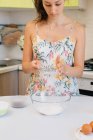 Жінка стоїть на кухні, просіюючи борошно в миску — стокове фото
