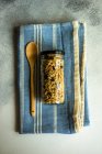 Frasco de vidro cheio de granola ao lado de uma colher de madeira em uma toalha de chá — Fotografia de Stock