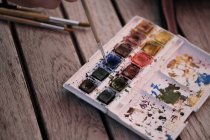 Watercolour paints and paintbrushes on a wooden table — Stock Photo