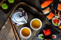 Plates of assorted maki sushi rolls and nigiri sushi on a table with green tea — Stock Photo