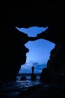 Vista desde una cueva de un hombre de pie sobre una roca en el mar, Islandia - foto de stock
