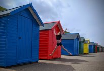 Jeune fille sautant dans les airs par des cabanes de plage, Whitby, Yorkshire, Angleterre, Royaume-Uni — Photo de stock