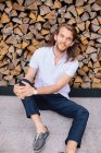 Retrato de un hombre guapo sentado en el suelo apoyado sobre una pila de troncos, Rusia - foto de stock