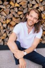 Portrait of a handsome man sitting on ground leaning against a log pile, Russia — Stock Photo