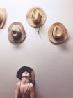 Smiling boy wearing a straw hat and looking up at straw hats hanging on a wall — Stock Photo