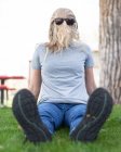 Женщина, сидящая в парке с покрытым волосами лицом и в солнечных очках, США — стоковое фото