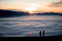 Silueta de dos mujeres en un pico de montaña al atardecer mirando a la vista, Salzburgo, Austria - foto de stock