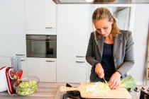 Mujer picando verduras en una cocina - foto de stock
