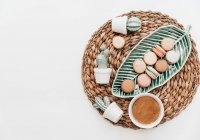 Macaroons on a leaf shaped dish, cactus decorations and a cup of coffee on a white background — Stock Photo
