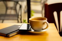 Tasse à café, ordinateur portable et téléphone portable sur une table dans un café — Photo de stock