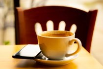 Кофейная чашка и мобильный телефон на столе в кафе — стоковое фото