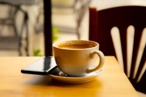 Tazza di caffè e telefono cellulare su un tavolo in una caffetteria — Foto stock