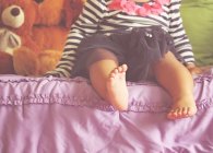 Close-up of a barefoot girl sitting on a bed — Stock Photo