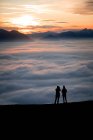 Silueta de dos mujeres en un pico de montaña al atardecer mirando a la vista, Salzburgo, Austria - foto de stock