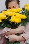 Primer plano de una mujer oliendo un ramo de crisantemos amarillos - foto de stock