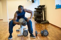 Чоловік сидить у спортзалі, піднімаючи ваги — стокове фото