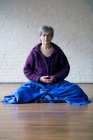 Retrato de uma mulher idosa sentada de pernas cruzadas meditando — Fotografia de Stock