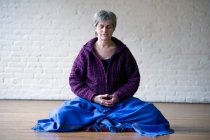 Retrato de una mujer mayor sentada con piernas cruzadas meditando - foto de stock