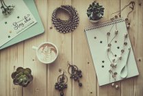 Cup of coffee with jewelry, plants and notepads on a table — Stock Photo