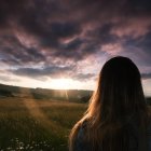 Rear view of a teenage girl standing in a field at sunset, France — Stock Photo