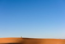 Vista lejana de un hombre bereber rezando en el desierto del Sahara, Marruecos - foto de stock
