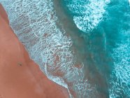 Luftaufnahme eines Mannes, der an der Sandküste in der Nähe von welligem Meer bei sonnigem Tag wandert — Stockfoto