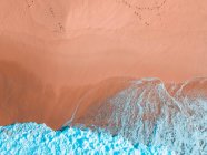 Воздушный вид на песчаное побережье около волнистого моря в солнечный день — стоковое фото