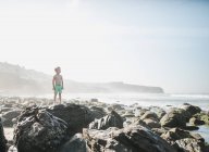Boy standing on rocks on the beach, Laguna Beach, California, Estados Unidos - foto de stock