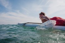 Adolescente acostado en una tabla de surf remando hacia el mar, Laguna Beach, California, Estados Unidos - foto de stock