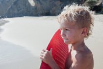 Retrato de un niño en la playa llevando un skimboard, Laguna Beach, California, Estados Unidos - foto de stock