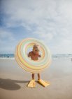 Boy standing on beach wearing diving flippers and an inflatable rubber ring, Laguna Beach, California, United States — Foto stock