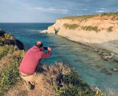 Чоловік, що стоїть біля моря, фотографує Мунксарра (Марсаскала, Мальта). — стокове фото