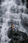 Mujer sentada en las rocas junto a una cascada, Bali, Indonesia - foto de stock