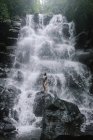 Mulher de pé sobre rochas por uma cachoeira, Bali, Indonésia — Fotografia de Stock