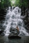 Donna seduta sulle rocce vicino a una cascata, Bali, Indonesia — Foto stock