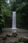Mulher sentada em rochas por uma cachoeira, Bali, Indonésia — Fotografia de Stock