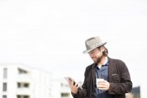 Портрет мужчины, стоящего на улице с чашкой кофе и цифровой табличкой — стоковое фото