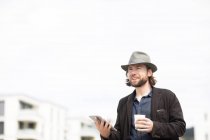 Портрет чоловіка, що стоїть на відкритому повітрі, тримає чашку кави та цифрового планшета — стокове фото