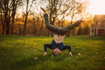 Funny little boy standing on head on green lawn — Stock Photo
