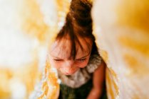 Overhead view of smiling girl with freckles covered with fabric and sunbeams on face — Stock Photo