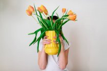 Cute little girl hiding behind vase of orange tulips — Stock Photo