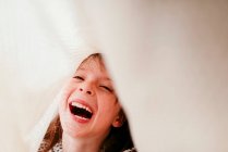 Laughing girl with freckles covered with fabric and sunbeams on face — Stock Photo