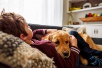 Мальчик обнимается с собакой на диване в гостиной — стоковое фото