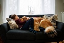 Menino abraçando com cão no sofá na sala de estar — Fotografia de Stock