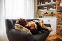 Хлопчик обіймається з собакою на дивані у вітальні — стокове фото