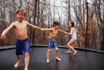 Three children jumping on a trampoline in the rain — Stock Photo