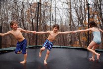 Троє дітей стрибають на батуті під дощем — стокове фото