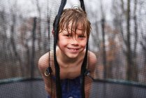 Porträt eines nassen und fröhlichen Kindes, das im Regen auf einem Trampolin spielt — Stockfoto