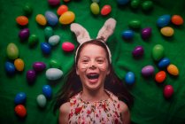 Retrato de arriba de una joven con orejas de conejo rodeada de huevos de Pascua - foto de stock